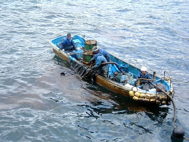 小型ボートに乗って流れ出た油を回収している作業員の写真